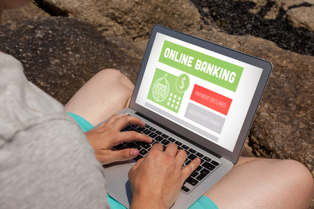 Online banking text on gray display against man sitting on the rocks and using laptop at the sea coastの写真素材