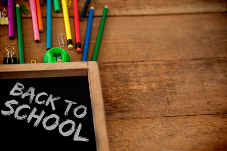 Graphic image of red back to school text against chalkboard with colored pencils on tableの写真素材