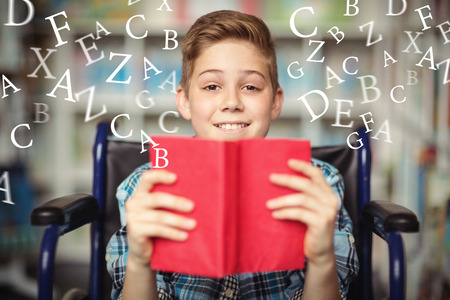 letters against portrait of disabled schoolboy holding book in libraryの写真素材