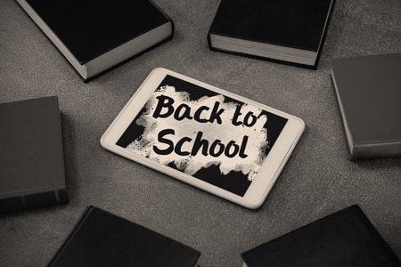 Back to school text on pink splash against digital tablet surrounded with colorful organizers on chalkboardの写真素材