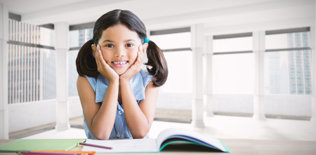Portrait of girl doing homework at desk against modern room overlooking cityの写真素材