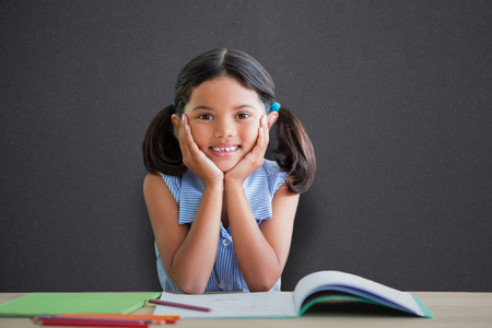 Portrait of girl doing homework at desk against black chalkboard