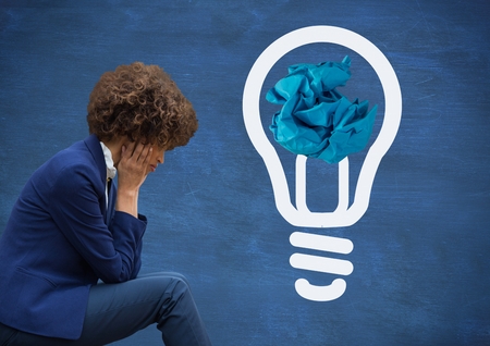 Digital composite of Woman sitting next to light bulb with crumpled paper ball in front of blackboardの写真素材