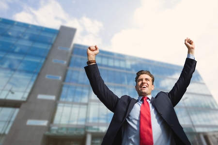 Digital composite of Excited business man standing against building backgroundの写真素材