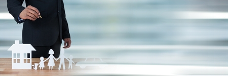 Digital composite of Man standing behind a table with paper figures as family, car and house insurance conceptの写真素材