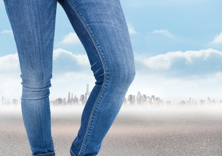 Digital composite of Woman's legs in front of city landscape in jeansの写真素材