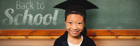 Portrait of smiling girl wearing mortarboard against blackboardの写真素材