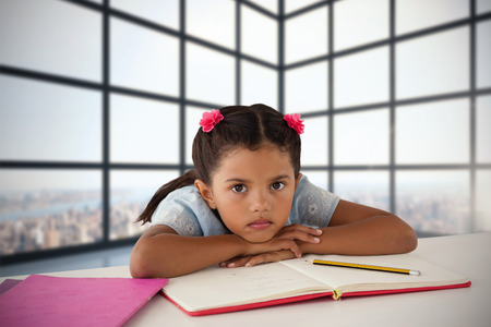 Girl leaning on open book at desk against room with large windows showing cityの写真素材