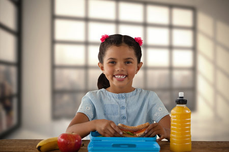 Smiling girl having sandwich at table against room with large window showing cityの写真素材