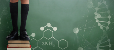 Low section of schoolboy standing on books against green chalkboardの写真素材