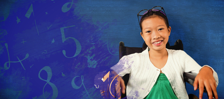 Young girl smiling while sitting on wheelchair against blue backgroundの写真素材