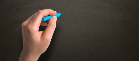 Hand holding blue chalk against blackboardの写真素材