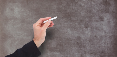 Hand holding a chalk and writing something against empty blackboard in schoolの写真素材