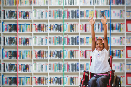 Girl in wheelchair in school corridor against multi colored bookshelf in libraryの写真素材