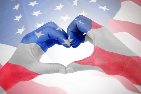 Woman making heart shape with hands against american flag with stars and stripesの写真素材