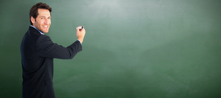 Businessman writing with marker while looking at camera against green chalkboardの写真素材
