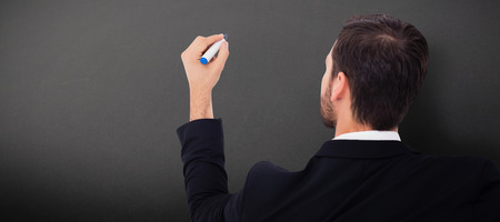 Rear view of businessman writing with marker against greyの写真素材