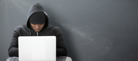 Focused male hacker using laptop  against grey