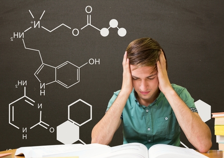 Digital composite of Worried student boy at table reading against grey blackboard with school and...