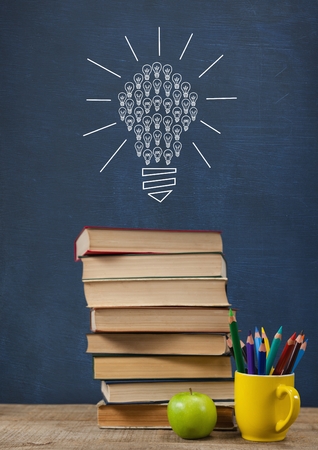 Digital composite of Books on the table against blue blackboard with bulb graphicの写真素材