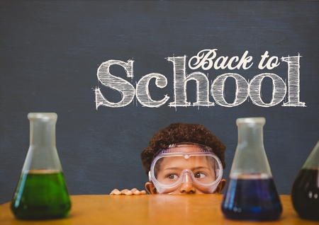 Digital composite of Student boy hiding behind a table against blue blackboard with back to school textの写真素材