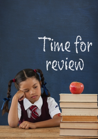 Digital composite of Bored student girl at table against blue blackboard with time for review textの写真素材