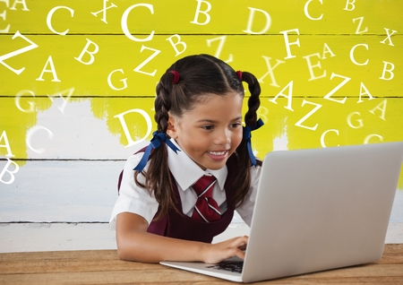Digital composite of Many letters around Schoolgirl on laptop with yellow painted backgroundの写真素材