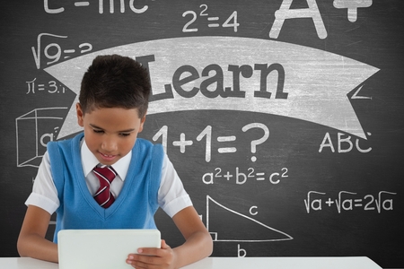 Digital composite of Student boy at table using a tablet against green blackboard with learn text and education and schooの写真素材
