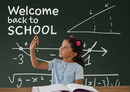 Digital composite of Student girl at table writing against green blackboard with welcome to school textの写真素材