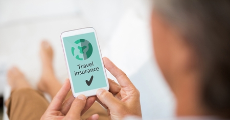 Digital composite of Man holding a phone with travel insurance concept on screenの写真素材