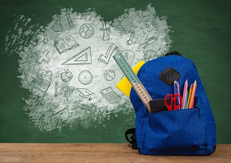 Digital composite of Schoolbag on Desk foreground with blackboard graphics of education icons drawingsの写真素材