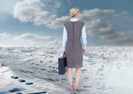 Digital composite of Businesswoman holding briefcase in sea of documents under sky cloudsの写真素材