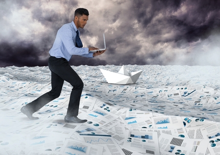 Digital composite of Businessman on laptop in sea of documents under sky clouds with paper boatsの写真素材