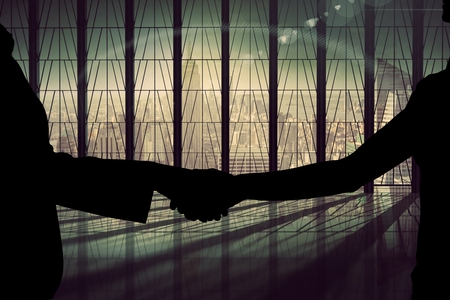 Digital composite of Business handshake silhouette against buildingの写真素材