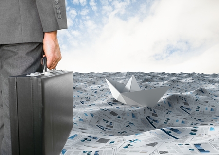 Digital composite of Businessman holding briefcase in sea of documents with paper boatの写真素材