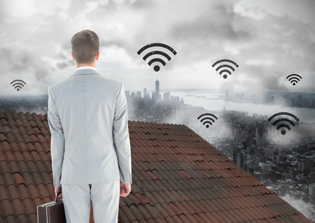 Digital composite of Wi-fi icons and Businessman standing on Roof with chimney and misty cityの写真素材