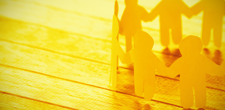 High angle view of yellow paper figures holding hands on wooden tableの写真素材