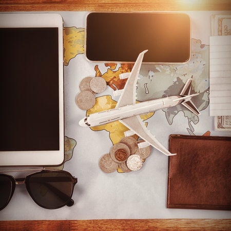 Overhead view of toy airplane by passport and currency with technologies on map at tableの写真素材