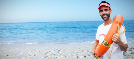 Portrait of male lifeguard holding life belt against beach against clear skyの写真素材