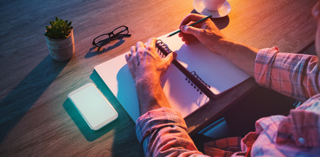 Cropped hands of businessman writing in diary at desk