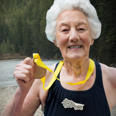 Portrait of female swimmer showing medal against river flowing in forestの写真素材