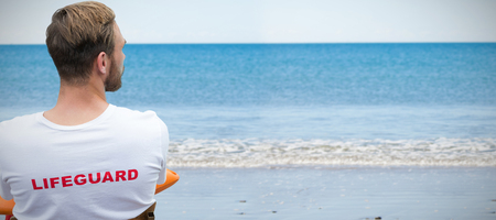 Rear view of male lifeguard against waters edge at the beachの写真素材