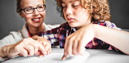 Teacher looking at boy using Braille to read in schoolの写真素材