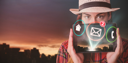 Portrait of woman hiding face with digital tablet  against city against cloudy sky during sunsetの写真素材