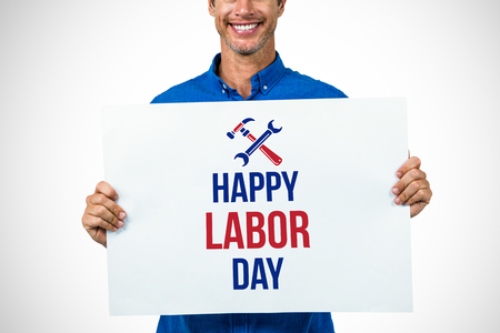 Portrait of happy man holding placard against digital composite image of happy labor day text with toolsの写真素材