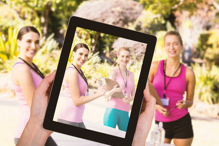 Close-up of hands holding digital tablet against portrait of young female volunteers with clipboardの写真素材
