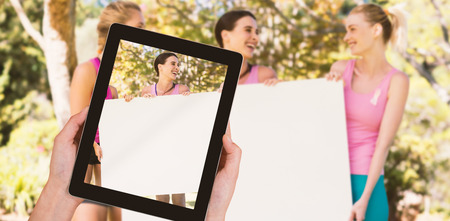 Close-up of hands holding digital tablet against volunteers holding blank sheet at parkの写真素材