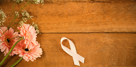 Directly above view of pink Breast Cancer Awareness ribbon by gerbera flowers on wooden tableの写真素材