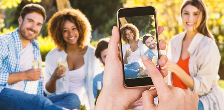 Hands touching smart phone against portrait of friends group having breakfast togetherの写真素材