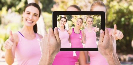 Cropped hand holding digital tablet against portrait of female volunteers showing thumbs up signの写真素材